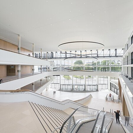 „Weitläufige Eingangshalle des CCH mit modernen Treppen, Glasfronten und einer großen runden Deckenleuchte.“