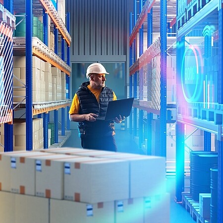 Person steht mit einem Laptop in einem großen Lagergang, umgeben von Regalen mit Kartons und farbigen Lichteffekten im Vordergrund.