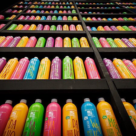 Regale voller bunter Flaschen, in mehreren Reihen angeordnet. Die Flaschen sind in kräftigen Farben wie Pink, Gelb, Grün, Blau und Orange gestaltet und tragen auffällige Schriftzüge.