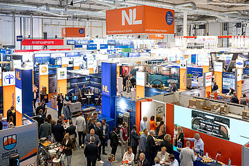 Blick über eine gut besuchte Messehalle der SMM mit zahlreichen Ausstellungsständen, Länderpavillons und Fachbesucherinnen und Fachbesuchern. Sichtbar sind unter anderem die Gemeinschaftsstände von Singapur, den Niederlanden, Griechenland und Japan.