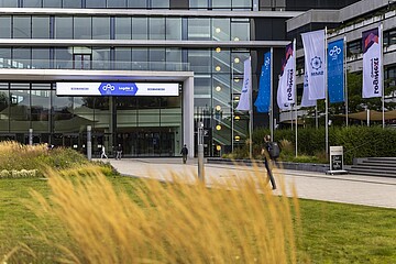 Eingangsbereich eines modernen Messe- und Veranstaltungsgebäudes mit Logistik-Event-Beschilderung und Fahnen vor einer großzügigen Glasfassade.