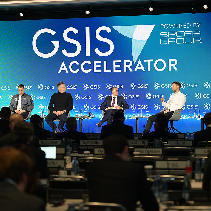 Podiumsdiskussion auf der GSIS Accelerator Conference vor einem großen, blau beleuchteten Bühnenhintergrund mit GSIS-Logo. Mehrere Teilnehmende sitzen auf der Bühne und diskutieren vor einem Publikum.