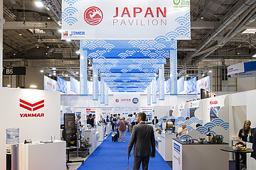 Blick durch den Japan Pavilion in einer Messehalle: Ein blauer Teppich führt durch Ausstellungsstände maritimer Unternehmen, darüber hängen Banner mit Wellenmotiven und der Aufschrift „Japan Pavilion“.