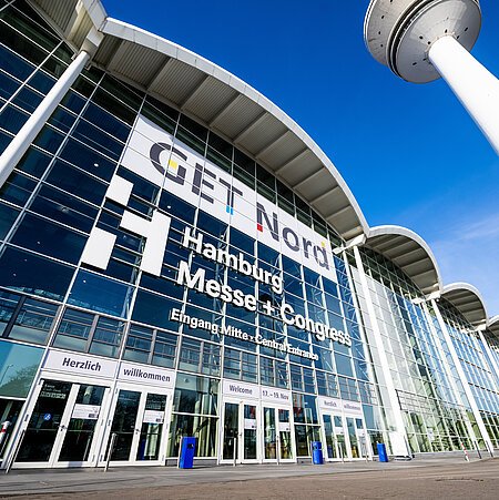 Der Eingang Mitte vom Zentralgebäude der Messe ist von außen aus der Froschperspektive abgebildet. Auf der Glasfront steht Get Nord und Hamburg Messe und Congress.