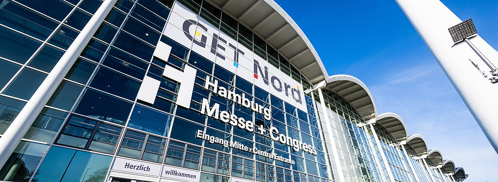Der Eingang Mitte vom Zentralgebäude der Messe ist von außen aus der Froschperspektive abgebildet. Auf der Glasfront steht Get Nord und Hamburg Messe und Congress.