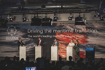 Podiumsdiskussion auf der SMM vor Publikum. Mehrere Sprecherinnen und Sprecher stehen auf einer Bühne vor einer großformatigen Veranstaltungswand zum Thema maritime Transformation.