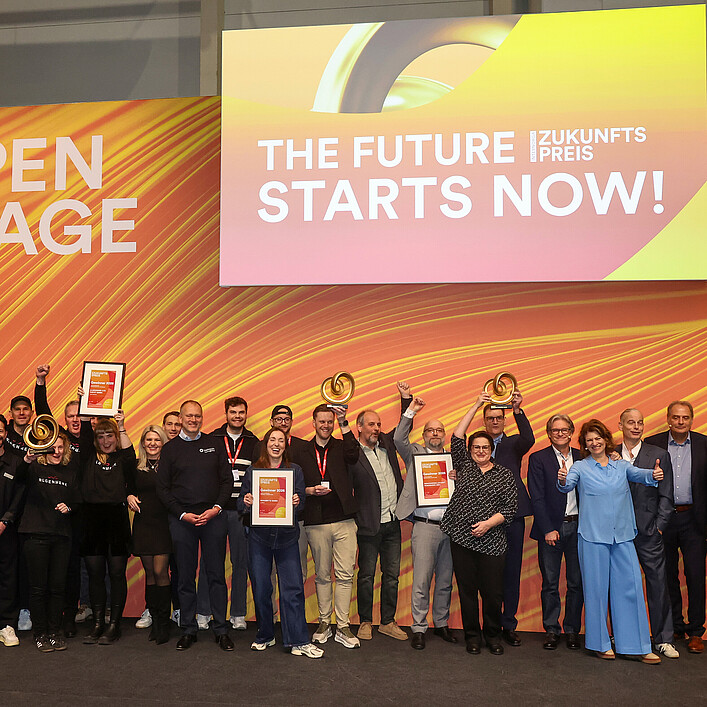 Gruppenfoto einer größeren Gruppe von ausgezeichneten Personen auf einer Bühne der Internorga. Sie halten Urkunden und Trophäen vor einer orange-gelben Bühnenkulisse mit der Aufschrift ‚Open Stage‘ und ‚The Future Starts Now!
