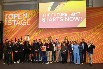 Gruppenfoto einer größeren Gruppe von ausgezeichneten Personen auf einer Bühne der Internorga. Sie halten Urkunden und Trophäen vor einer orange-gelben Bühnenkulisse mit der Aufschrift ‚Open Stage‘ und ‚The Future Starts Now!